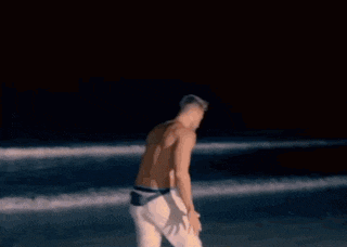 a shirtless man is standing on a surfboard on the beach