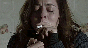 a woman is crying while smoking a cigarette in a dark room .
