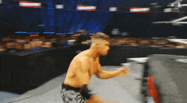 a man without a shirt is standing in a wrestling ring with his arms outstretched .