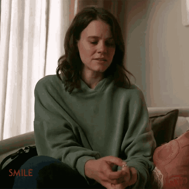 a woman in a green sweatshirt sits on a couch