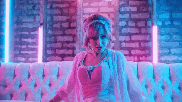 a woman in a pink dress is sitting on a white couch in front of a brick wall .