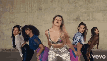 a group of women are dancing in front of a wall with the word vevo in the corner .