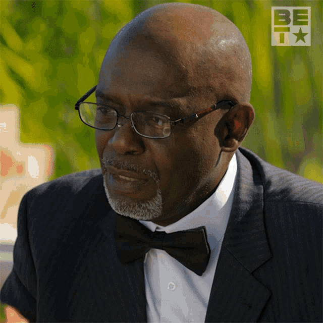 a man wearing glasses and a bow tie has the word be on the bottom right