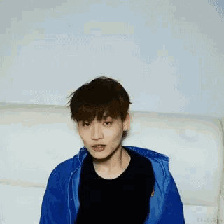 a young man is sitting on a couch wearing a blue jacket .