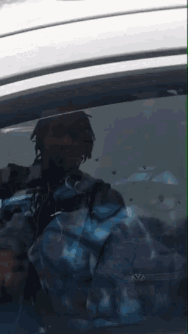 a man in a blue jacket is reflected in the windshield of a silver car