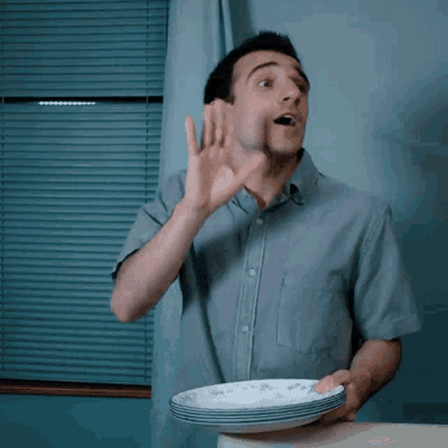 a man in a grey shirt is holding a stack of plates in front of a window