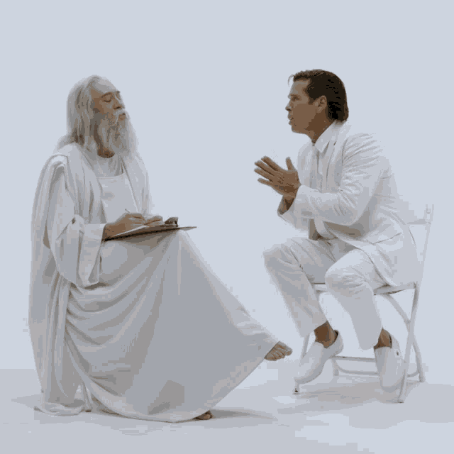 a man in a white robe is kneeling down next to a man in a white suit