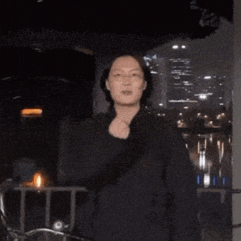 a man in a black shirt and glasses is standing in front of a city at night
