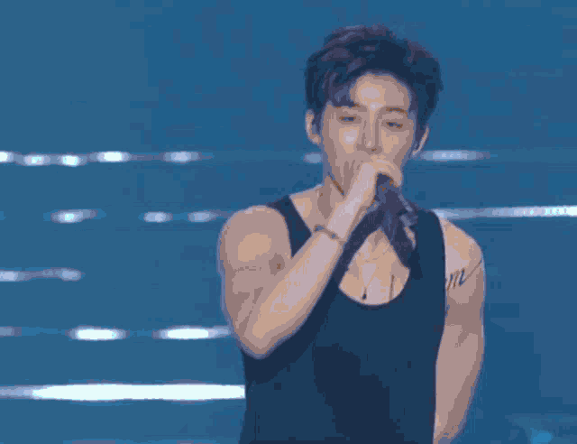 a man in a black tank top singing into a microphone with the word me on his chest