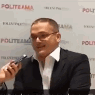 a man in a suit is talking into a microphone while wearing glasses