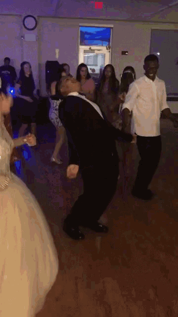 a group of people are dancing in a room with a red exit sign