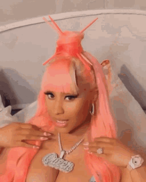 a woman with long pink hair is laying on a bed with her arms in the air .