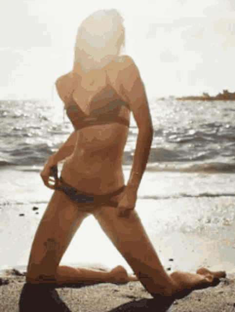 a woman in a bikini is kneeling on the beach near the ocean