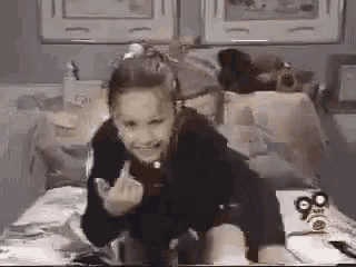 a little girl is sitting on a bed and giving a middle finger .