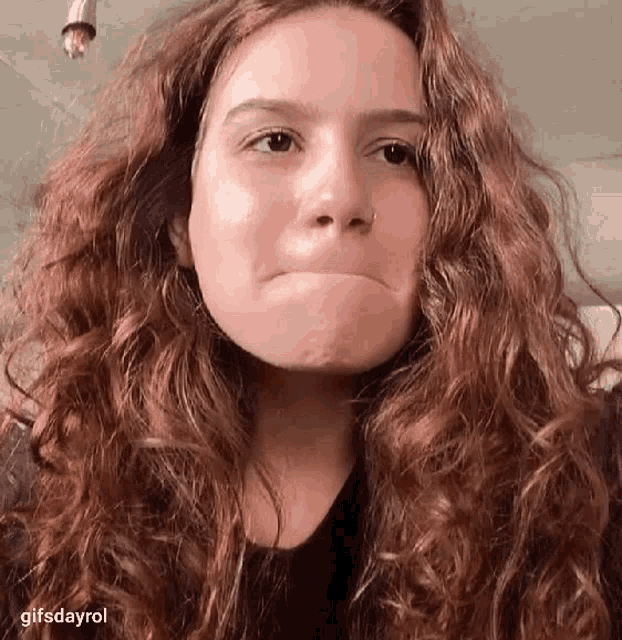 a woman with long curly hair is making a funny face with her mouth open .