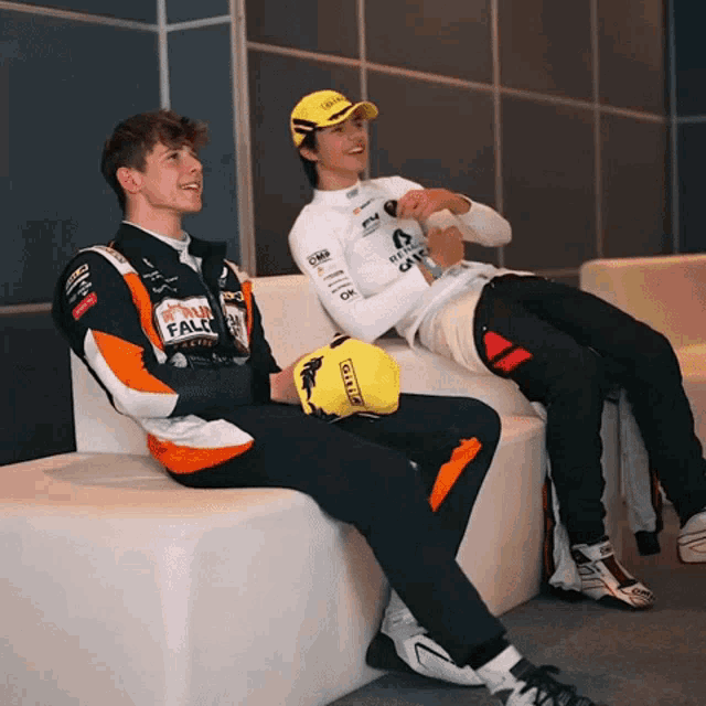 two racers are sitting on a couch with one wearing a jacket that says ' ferrari falls ' on it