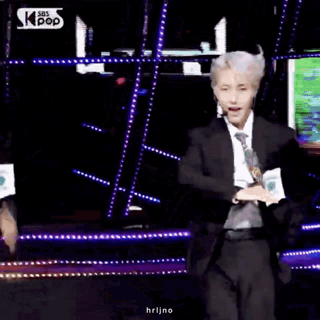 a man in a suit and tie is dancing on a stage in front of a sign that says sbs kpop