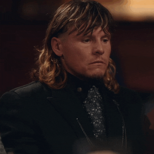 a man with long hair is wearing a black suit and a tie