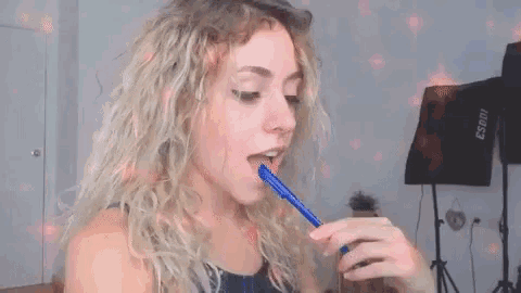 a woman with blonde hair is holding a blue pen in her mouth