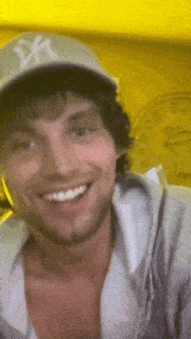 a man wearing a hat and a hoodie is smiling in front of a yellow wall clock .