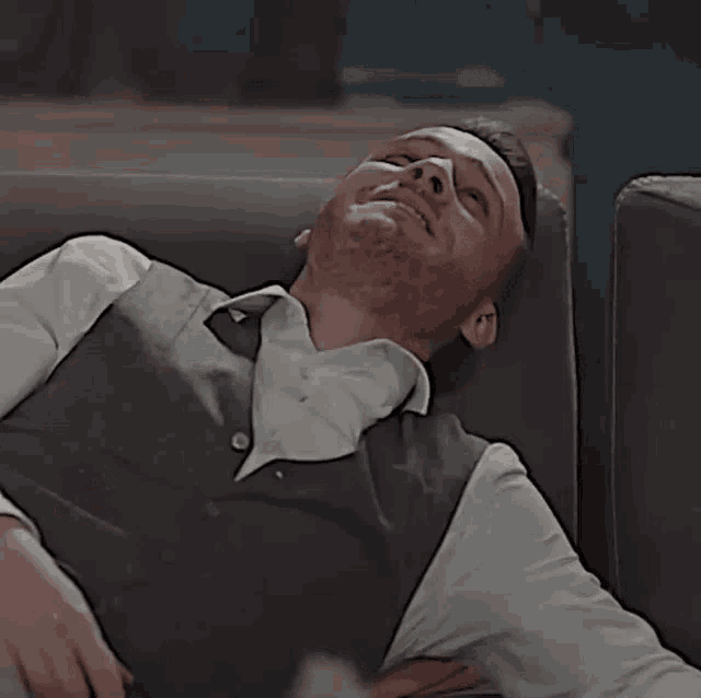 a man in a vest is laying on a couch and laughing