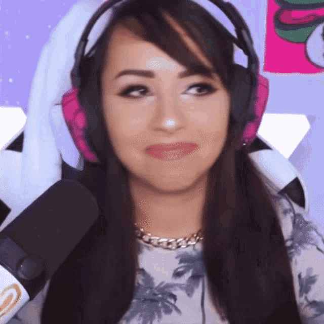 a woman wearing headphones and a necklace is sitting in front of a microphone and making a funny face .