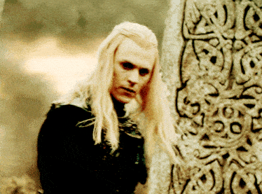 a man with long blonde hair is standing in front of a stone carving