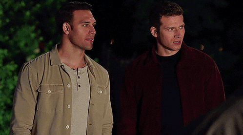 two men standing next to each other with one wearing a red jacket