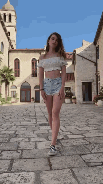 a woman in a white off the shoulder top and denim shorts