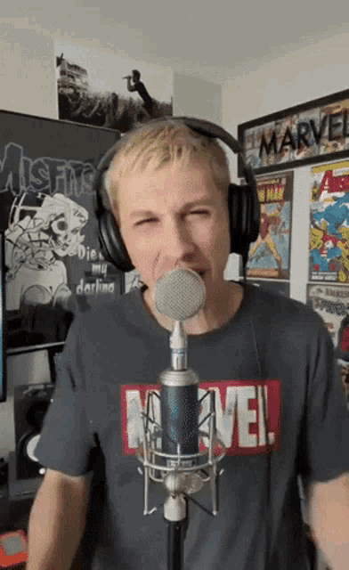 a man wearing headphones and a marvel shirt is singing into a microphone ..