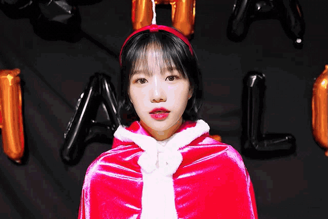 a girl in a red cape stands in front of balloons that spell out halloween