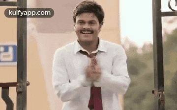 a man in a white shirt and red tie is clapping his hands in front of a building .