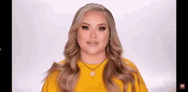 a woman wearing a yellow sweater and a gold necklace with a smiley face on it