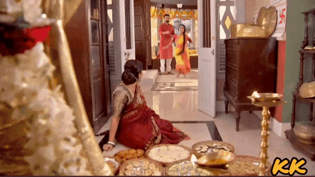 a woman in a red sari sits on the floor in front of a tray of food