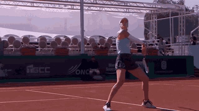 a woman is playing tennis on a court with a banner for tgcc in the background