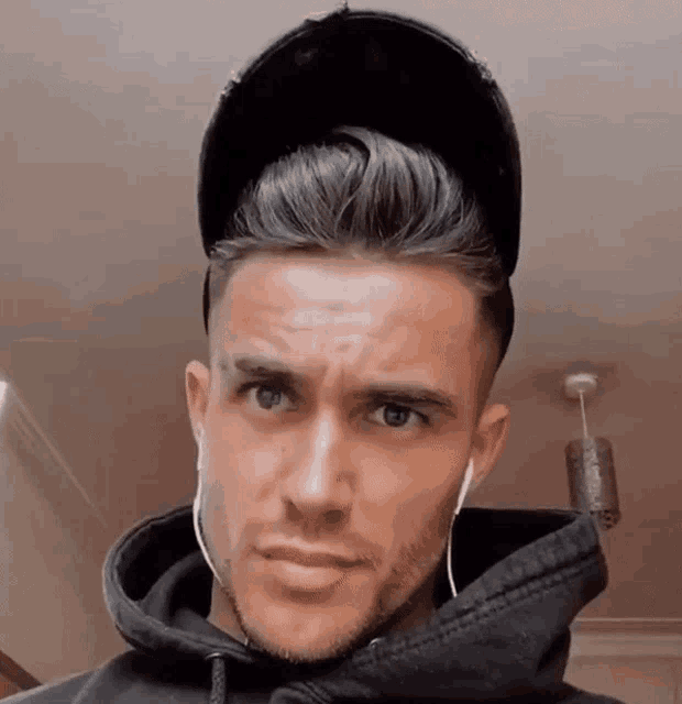 a man wearing a hat and headphones looks at the camera with a serious look on his face