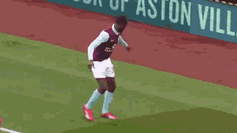a soccer player is jumping in the air in front of a sign that says aston villa
