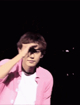 a young man wearing a pink shirt and a white t-shirt is waving at the camera .
