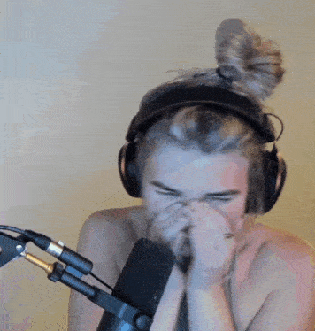 a shirtless man wearing headphones covering his nose in front of a microphone