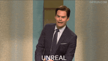 a man in a suit and tie stands in front of a wall with the word unreal on it