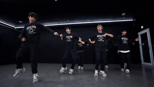 a group of young men are dancing in a dark room and one of them is wearing a shirt that says new york university