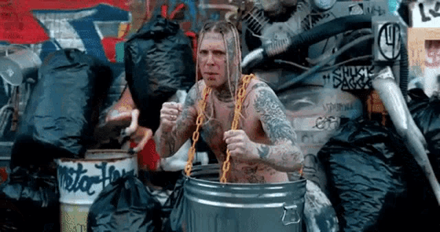 a shirtless tattooed man is standing in a trash can .
