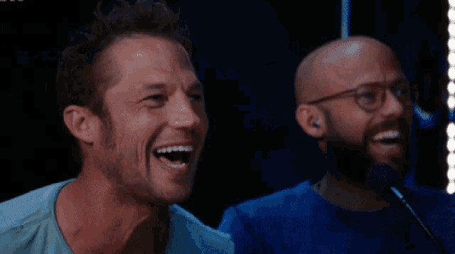 a man with glasses and a ring on his finger smiles next to another man