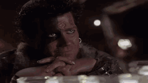 a man with a tattoo on his face is sitting at a table with his hands folded