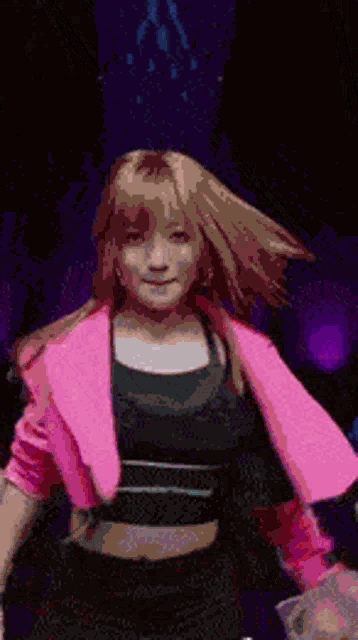 a woman wearing a pink jacket and a black top is dancing on a stage .