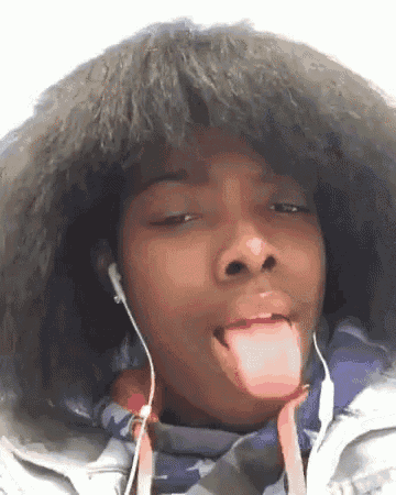 a young girl wearing headphones and a jacket is sticking out her tongue .