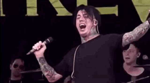 a man with tattoos is singing into a microphone on stage .