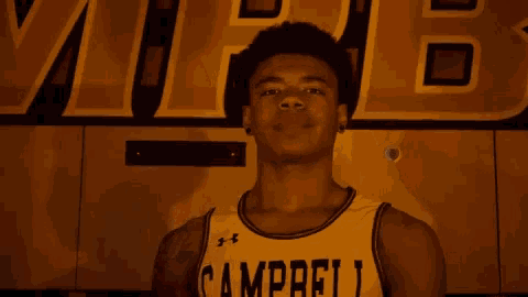a young man wearing a campbell jersey stands in front of a yellow wall