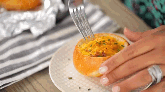 a person is holding a fork in a bread bowl filled with food .