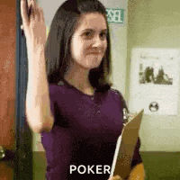 a woman in a purple shirt is holding a clipboard and waving at the camera .